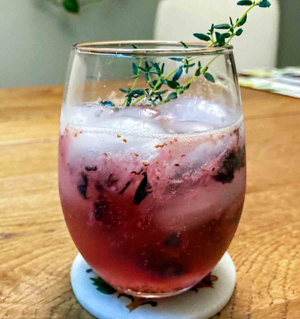 A glass of blueberry prosecco spritz with sprigs of thyme for garnish.