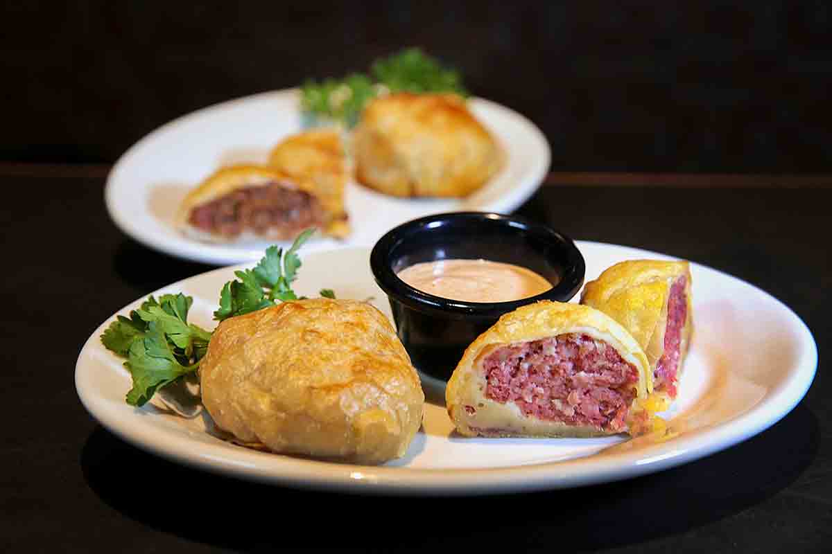 Two Boston knishes filled with corned beef, sauerkraut with a dish of Russian dressing on the side.