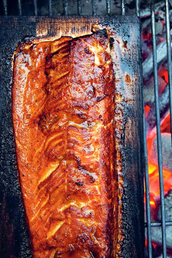 Half of a whole salmon on a cedar plank over glowing coals.