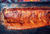 Half of a whole salmon on a cedar plank over glowing coals.