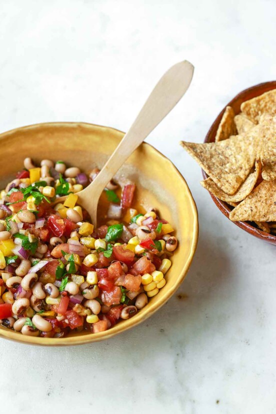 A yellow bowl filled with cowboy caviar salad with a bowl of tortilla chips on the side.