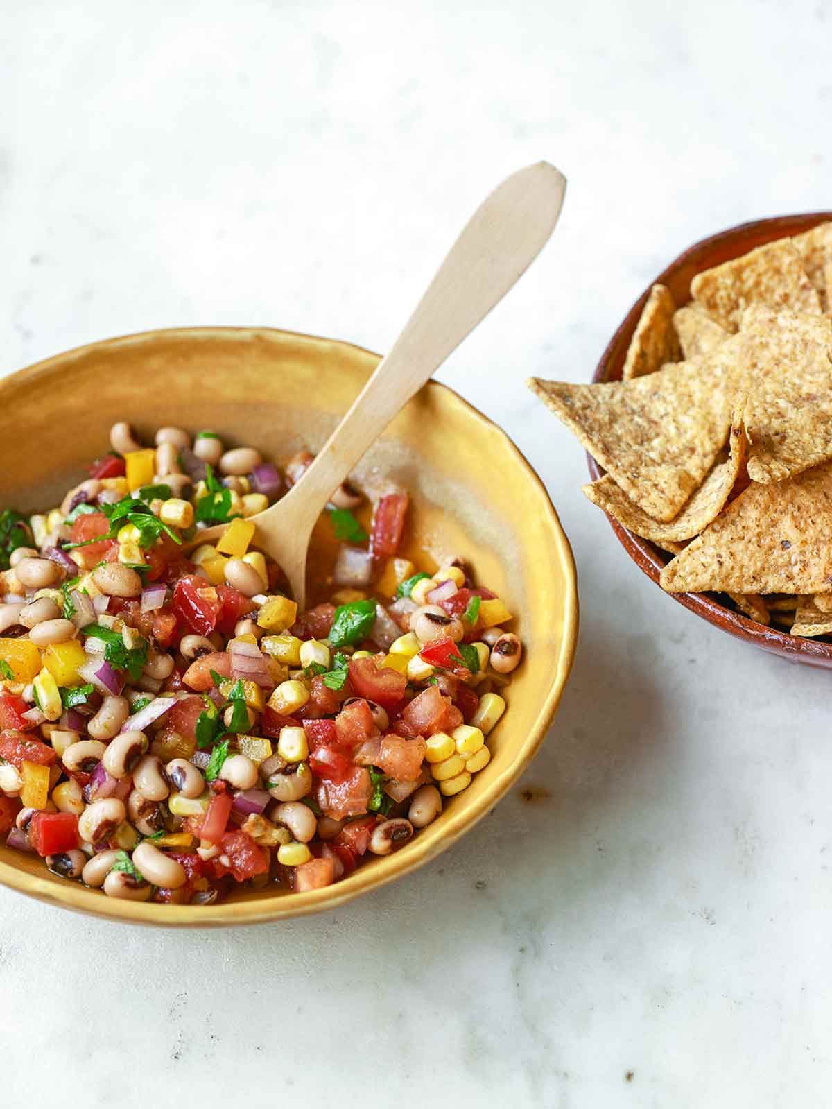 A yellow bowl filled with cowboy caviar salad with a bowl of tortilla chips on the side.