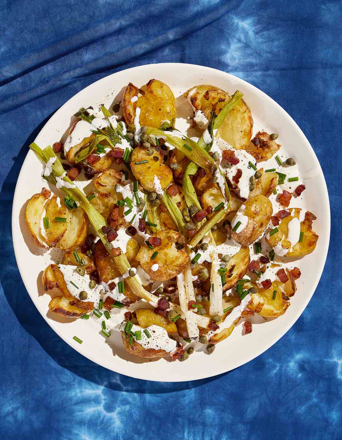 A white plate topped with crispy smashed potato salad sprinkled with pancetta and chives and topped with a creamy dressing.