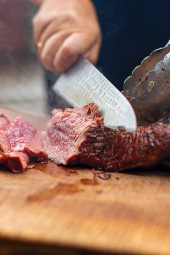 A person slicing a dry-rubbed tri tip on a wooden board.