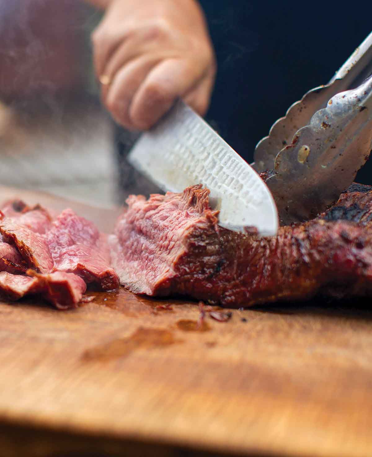 A person slicing a dry-rubbed tri tip on a wooden board.