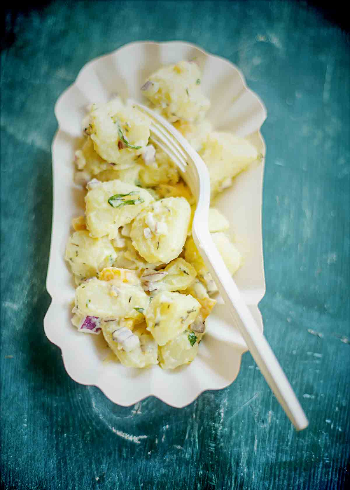 A cardboard bowl filled with easy potato salad an a plastic fork resting on top.