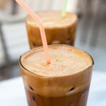 Two tall glasses filled with Greek-style frappe, with colorful straws standing up in them.