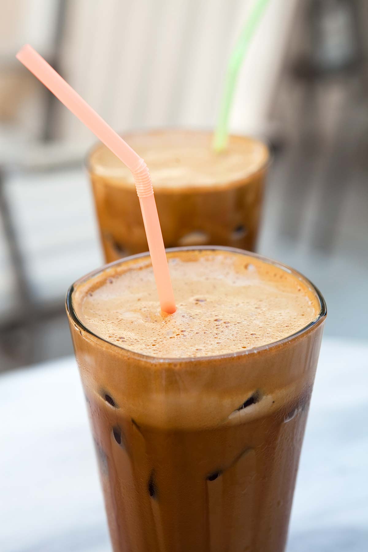 Two tall glasses filled with Greek-style frappe, with colorful straws standing up in them.