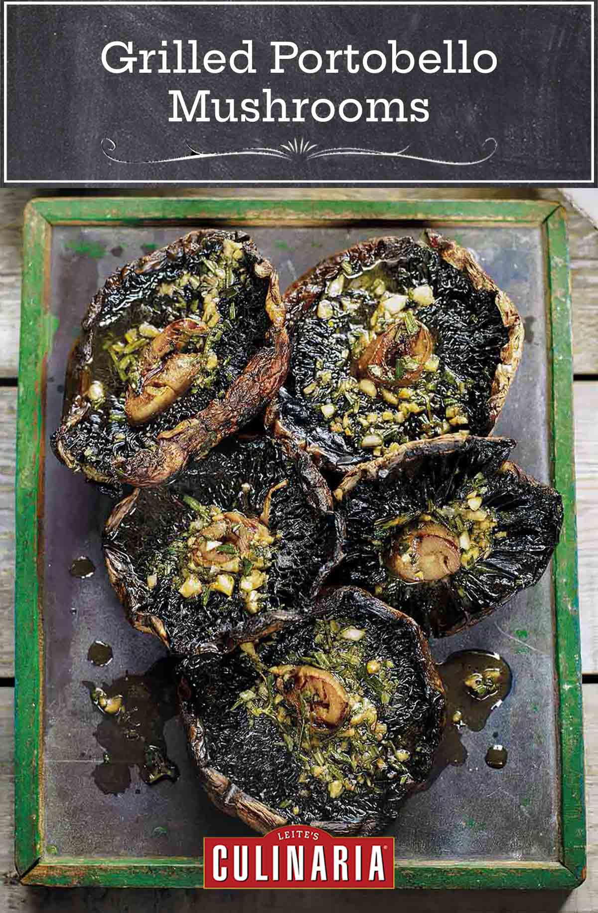 A metal platter holding five grilled portobello mushrooms, topped with garlic rosemary butter.