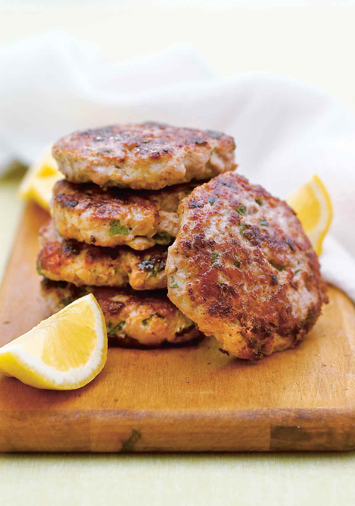 A stack of four ground turkey sliders plus one resting on its side with lemon wedges on a cutting board.