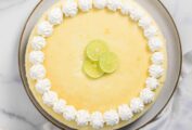 A whole key lime cheesecake with pecan crust topped with lime slices and whipped cream on a plate.