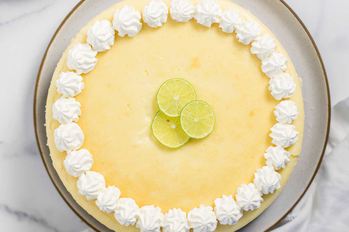 A whole key lime cheesecake with pecan crust topped with lime slices and whipped cream on a plate.