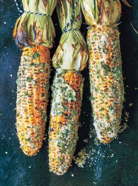 Three ears of grilled Mexican-style street corn slathered with lime mayo and sprinkled with cilantro, cheese, hot sauce.