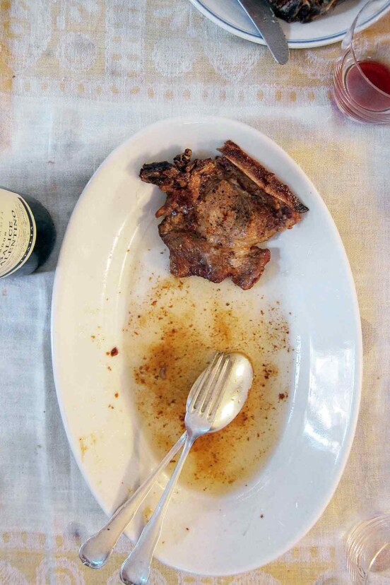 A piece of pan-seared pork chop on a white oval platter with a fork and spoon resting in butter sauce on the platter.