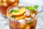 Two glasses of peach iced tea with mint leaves and peach slices for garnish.