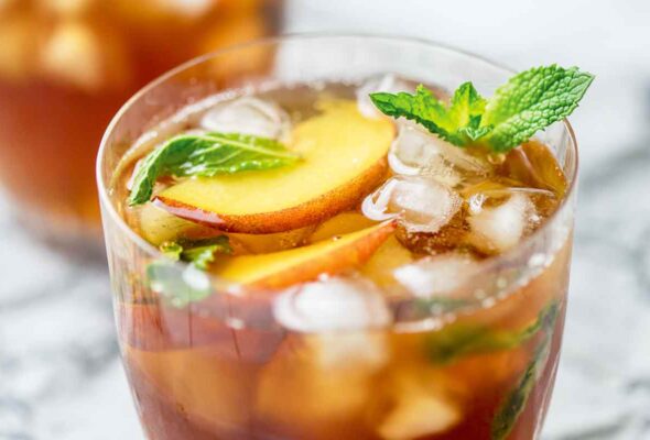 Two glasses of peach iced tea with mint leaves and peach slices for garnish.