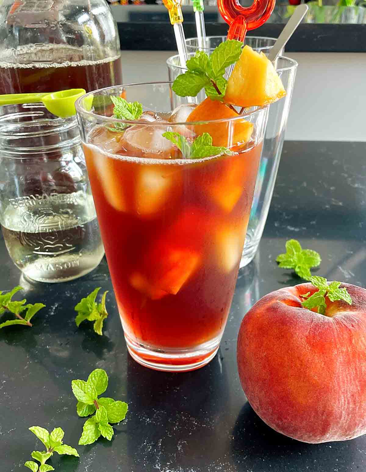 A glass of peach iced tea with min springs and a peach on the side.