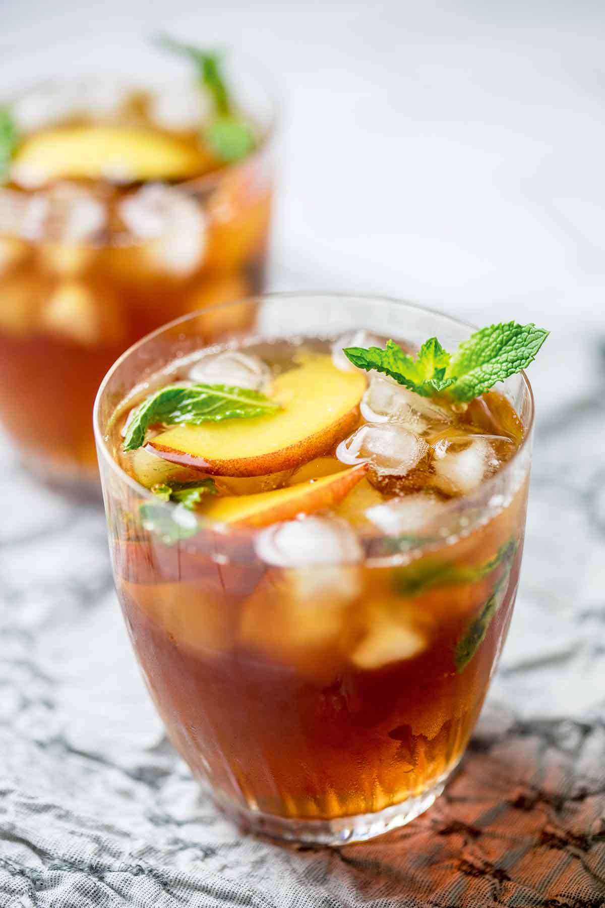 Två glas persika iste med myntablad och persikoskivor till garnering.