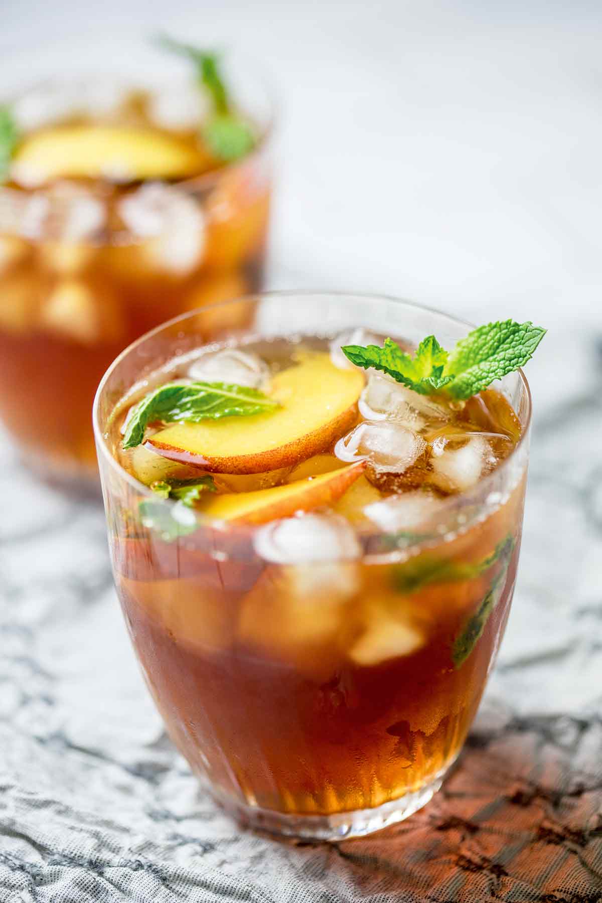 Two glasses of peach iced tea with mint leaves and peach slices for garnish.