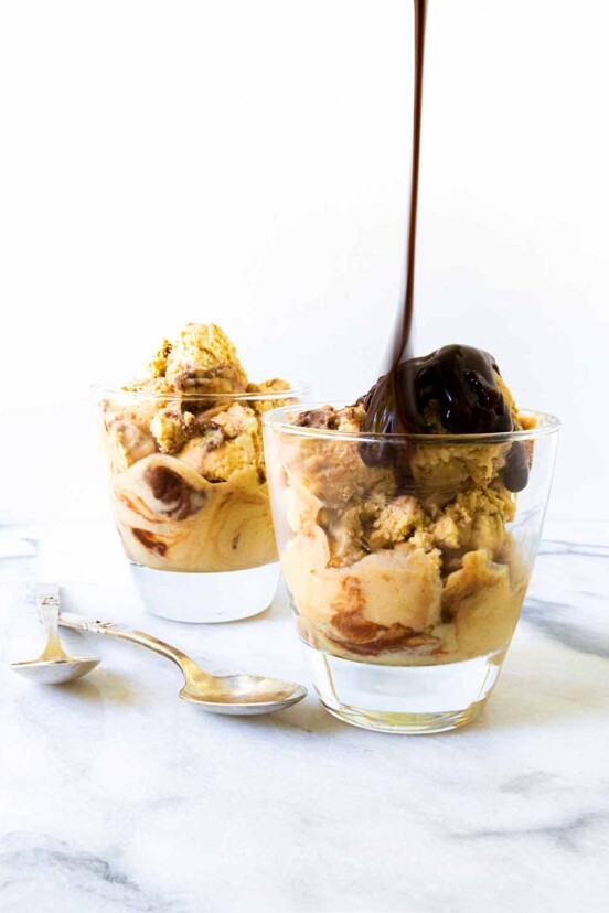 Two glasses filled with peanut butter ice cream with Nutella fudge swirled through and poured on top and two spoons on the side.