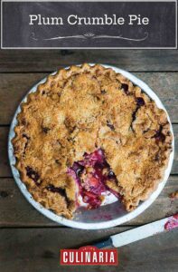 A baked plum crumble pie with a serving cut from it and a knife on the table beside it.