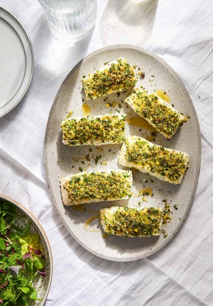 Six fillets of quick baked fish with bread crumbs and herbs on top on an oval platter.