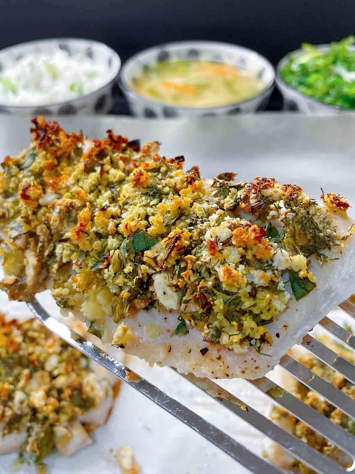 A fish spatula holding a fillet of quick baked fish with bread crumbs and herbs on top.
