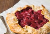 A raspberry crostata--a rustic tart with the crust folded over a filling of raspberries--on a sheet of parchment.