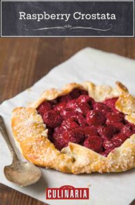 A raspberry crostata--a rustic tart with the crust folded over a filling of raspberries--on a sheet of parchment.