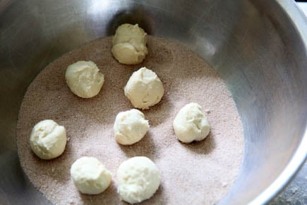 Balls of monkey bread dough being rolled in cinnamon sugar.