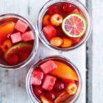 Three glasses filled with rosé sangria, lime wheels, nectarine wedges, watermelon cubes, and raspberries.