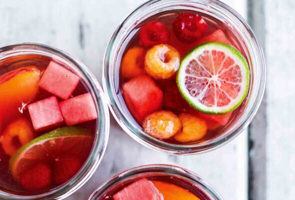 Three glasses filled with rosé sangria, lime wheels, nectarine wedges, watermelon cubes, and raspberries.