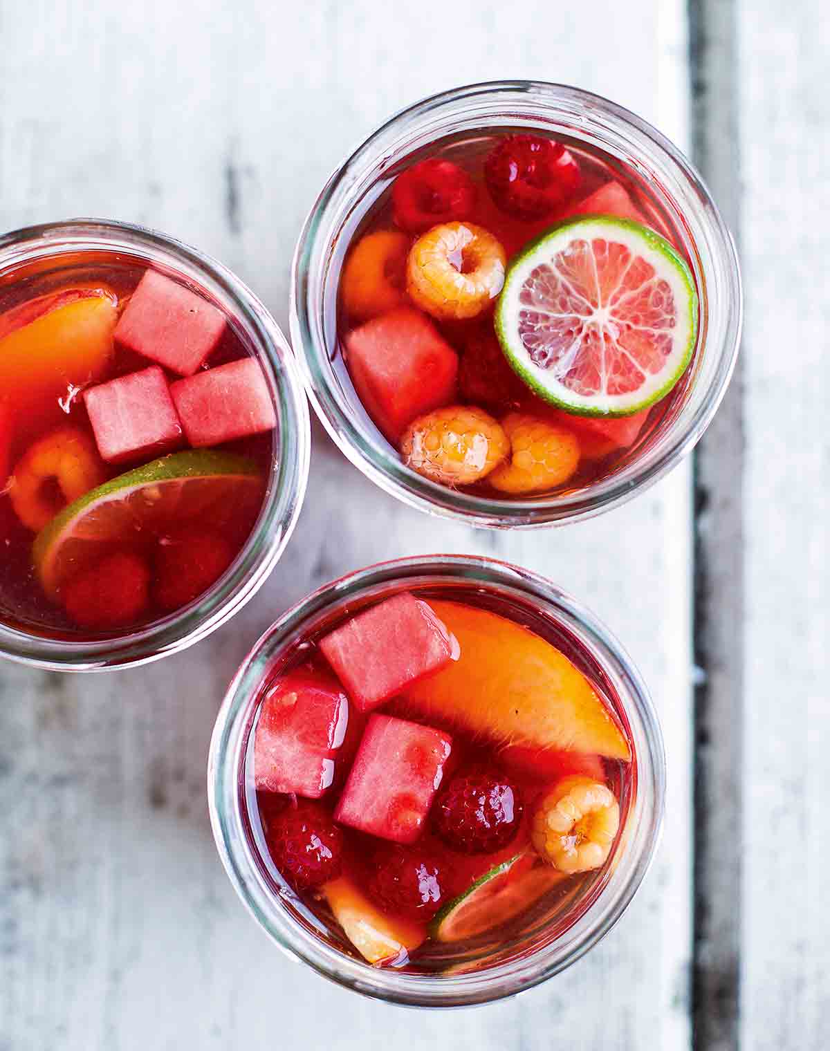 Three glasses filled with rosé sangria, lime wheels, nectarine wedges, watermelon cubes, and raspberries.