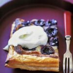 A square of rustic cherry puff pastry tart, topped with a dollop of whipped cream.