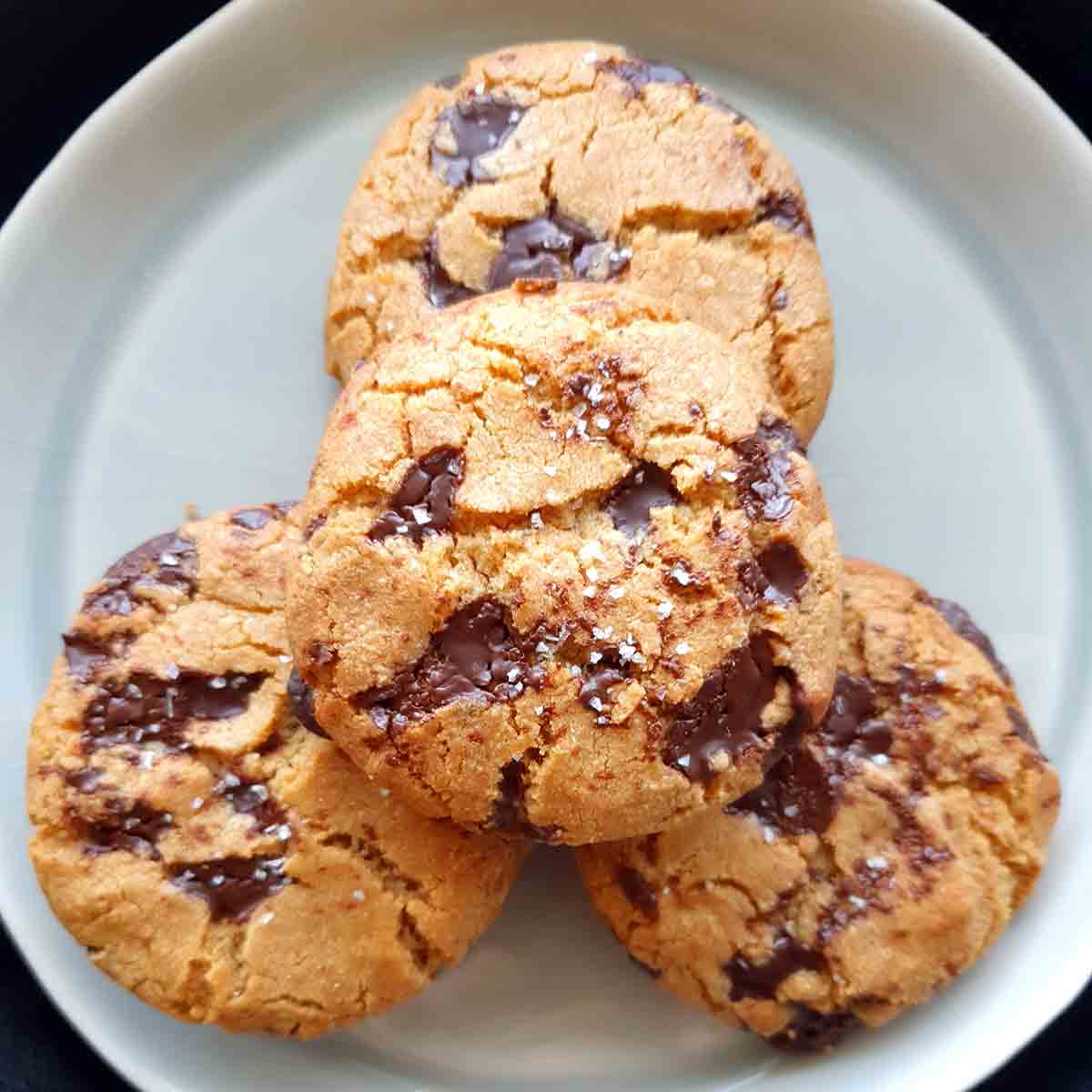 Four salted brown butter chocolate chunk cookies on a white plate.