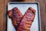 Two slabs of smoked ribs on a rimmed baking sheet with spicy bourbon bbq sauce in a dish on the side.