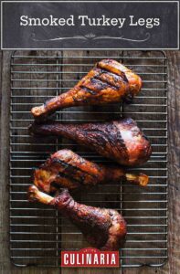 Four smoked turkey legs on a wire rack on a wooden surface.