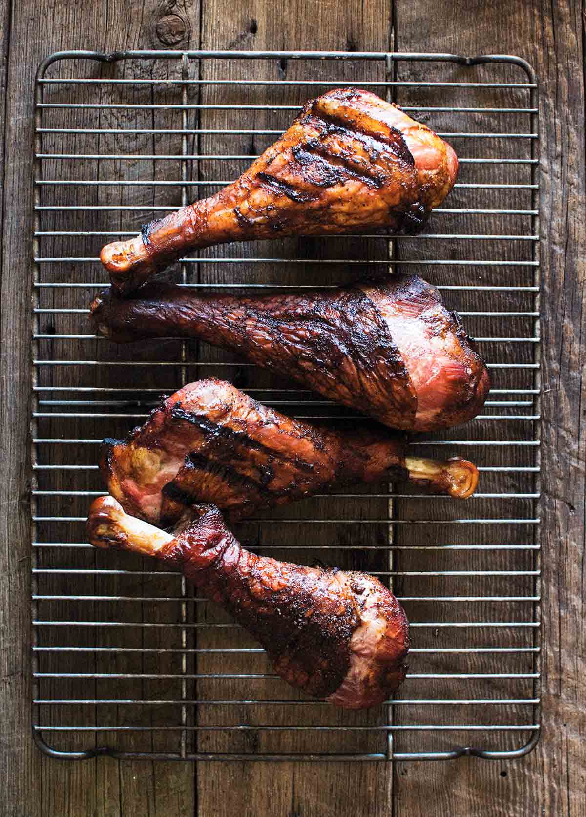 Four smoked turkey legs on a wire rack on a wooden surface.