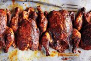 Four smoked whole chickens on a metal sheet pan with a metal fork lying beside them.
