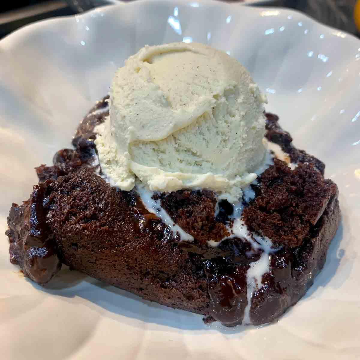 A serving of spicy hot fudge pudding cake in a white bowl topped with a scoop of ice cream.