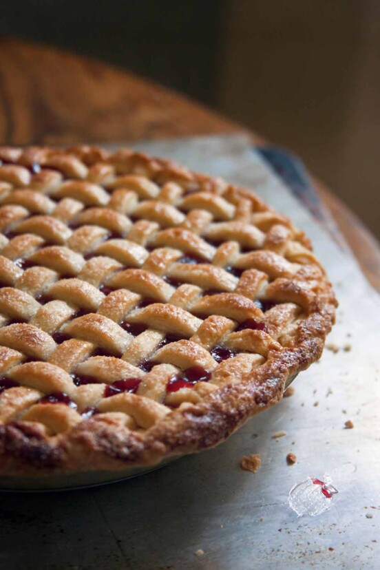 A whole sweet cherry pie with a lattice crust on a baking sheet on a wood table.