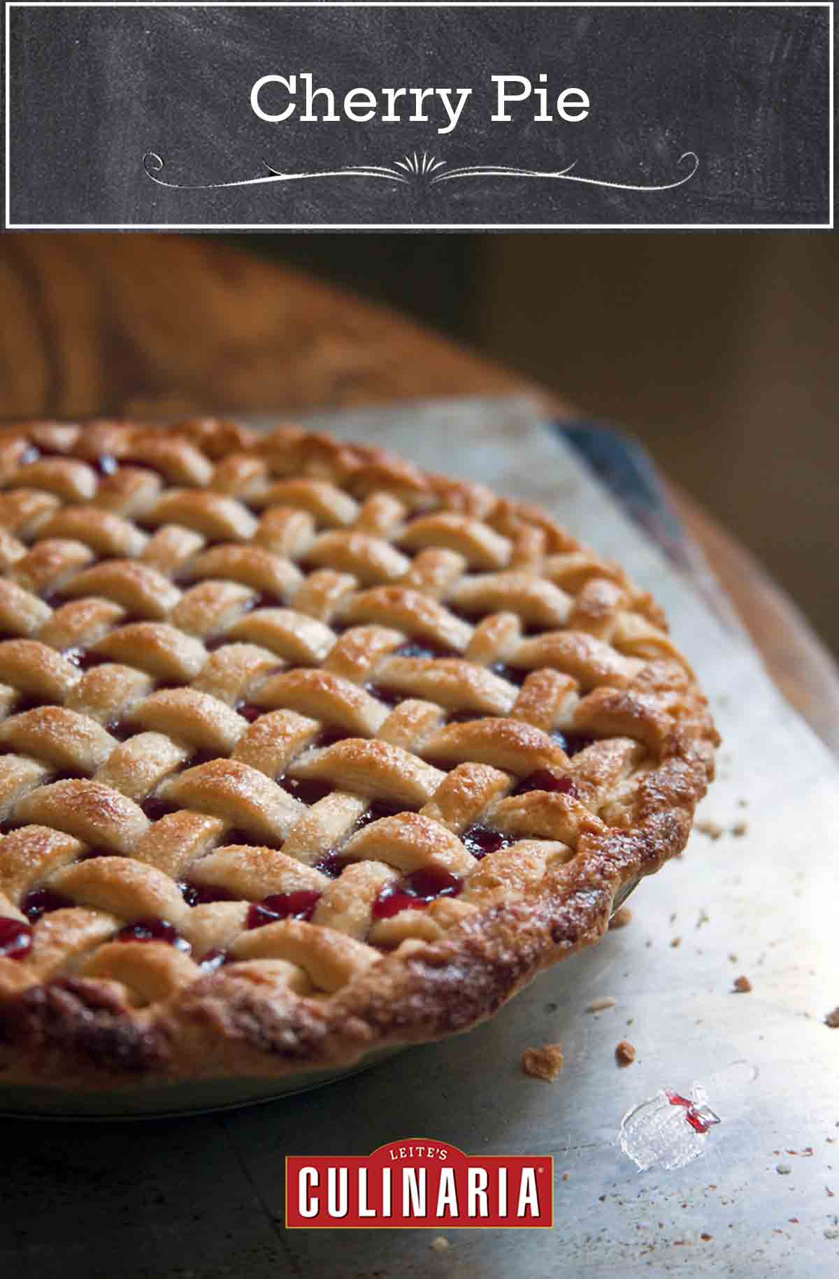 A whole sweet cherry pie with a lattice crust on a baking sheet on a wood table.