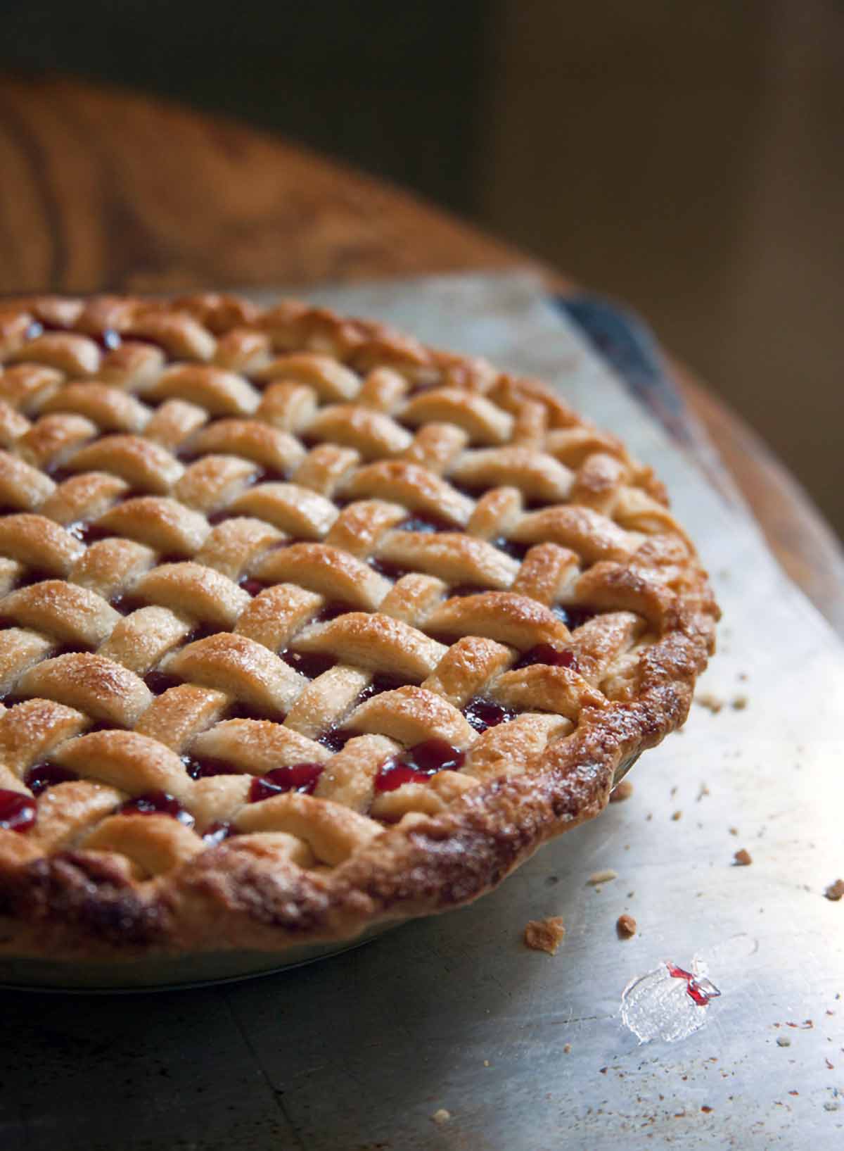 A whole sweet cherry pie with a lattice crust on a baking sheet on a wood table.