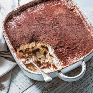 A square baking dish filled with traditional Italian tiramisu with a spoon resting inside and a portion missing.