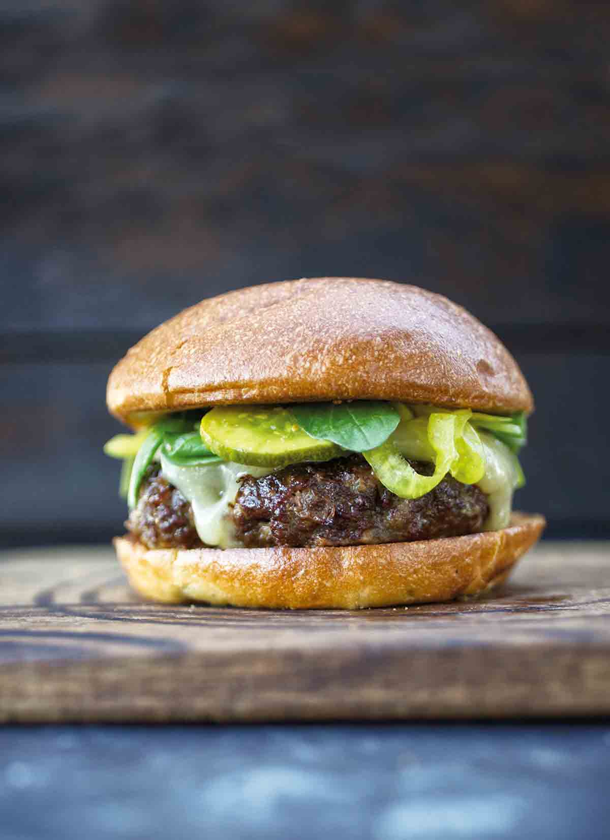 A vension burger with cheese, pickles, and arugula on a wooden board.