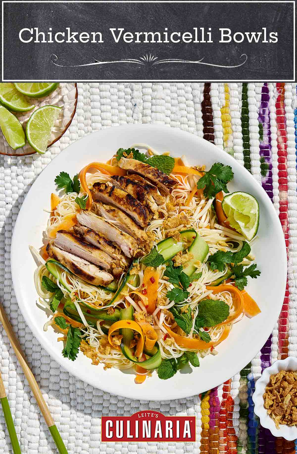 A white plate topped with vermicelli noodles, chicken, and raw vegetables with chopsticks and lime wedges on the side.