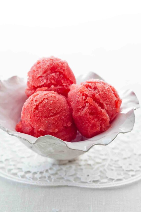 Three scoops of watermelon sorbet in a white serving dish.