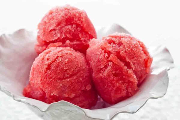 Three scoops of watermelon sorbet in a white serving dish.
