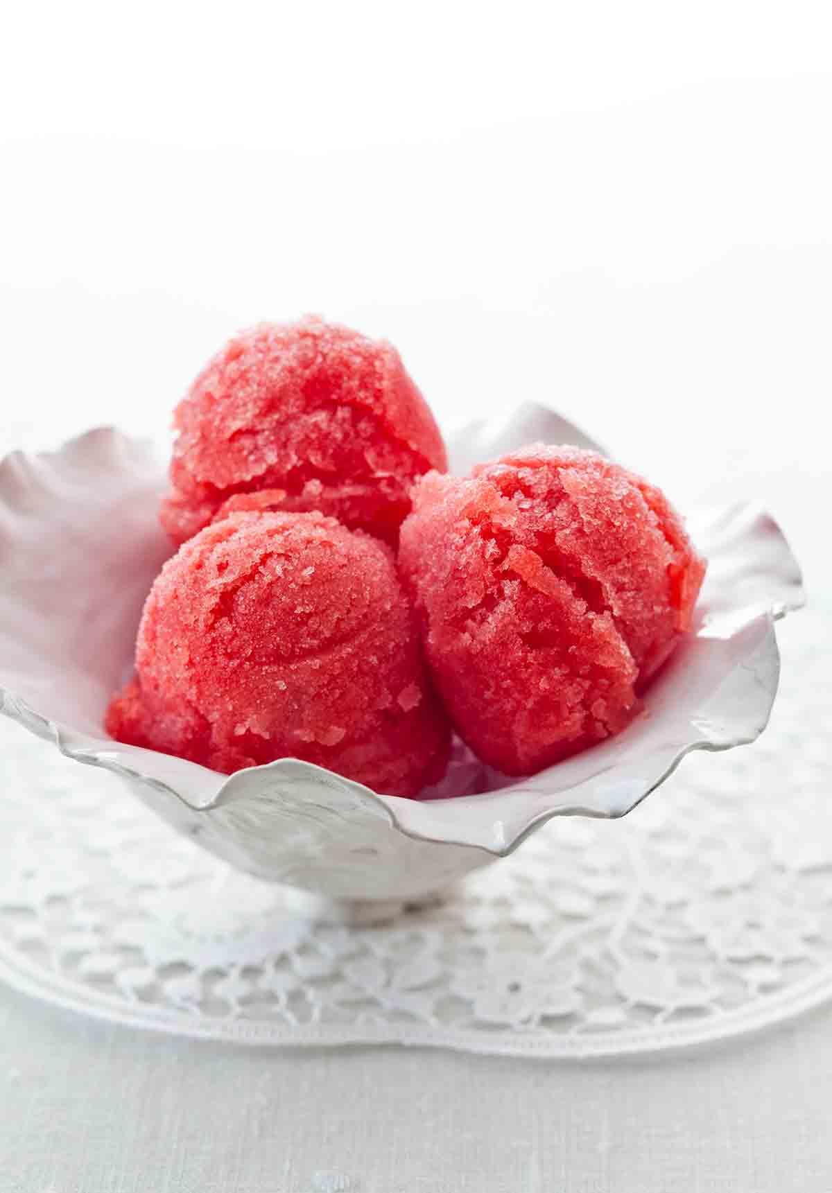 Three scoops of watermelon sorbet in a white serving dish.