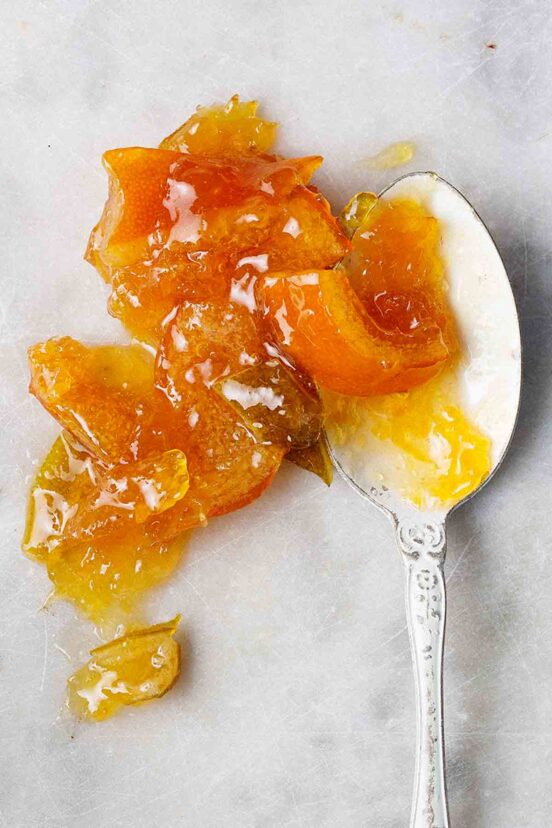 A spoonful of mixed citrus marmalade spilling over onto a grey marble surface.